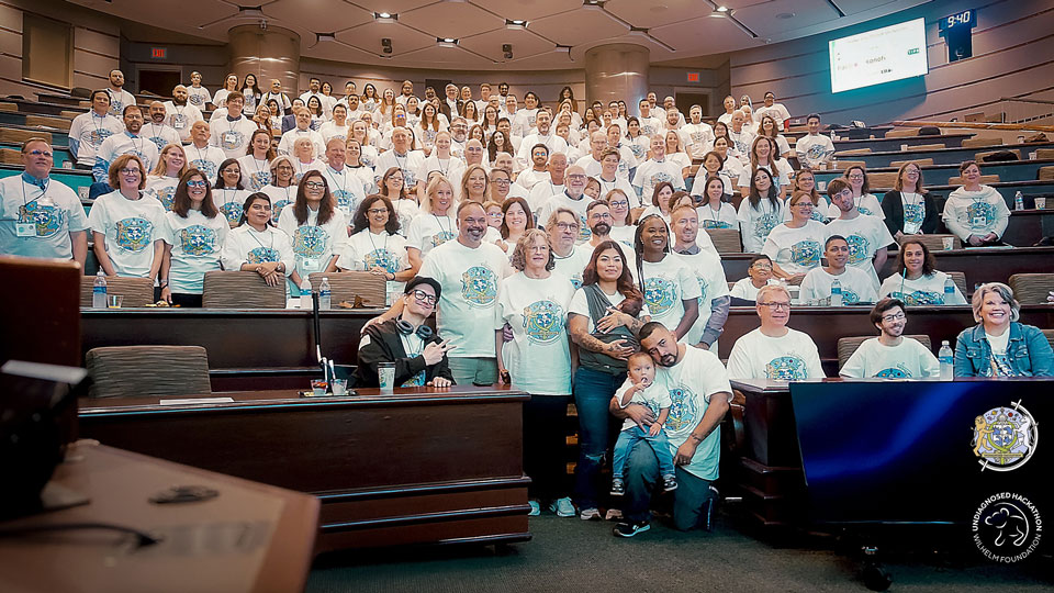 Large group photo of clinicians, researchers, data scientists, families and collaborators gathered in a lecture hall at Mayo Clinic, all wearing matching Undiagnosed Hackathon T-shirts, at the 3rd Undiagnosed Hackathon 2025
